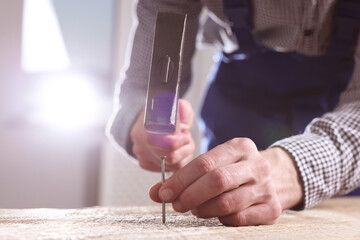 Professional repairman hammering nail into wooden board indoors, closeup