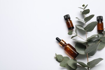 Aromatherapy. Bottles of essential oil and eucalyptus branches on white background, flat lay. Space for text