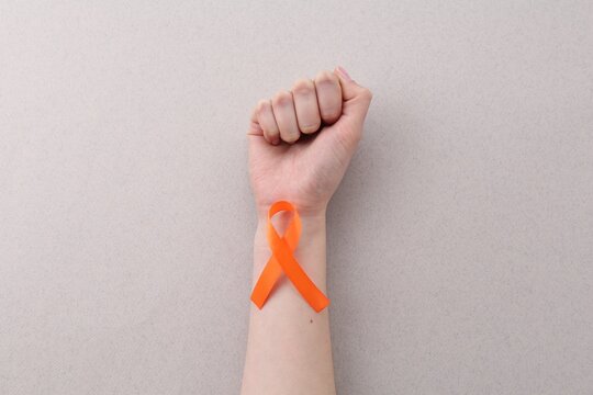 Woman with orange awareness ribbon on gray background, top view