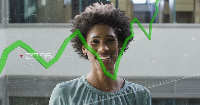 Image of graphs with changing numbers over smiling african american woman standing in office