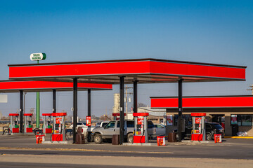 Gas station with bright red overhead roof on sunny day and cars and pick up trucks filling up with...