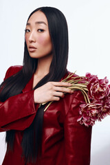 Stylish Asian woman in red leather jacket holding bouquet of pink flowers in urban setting