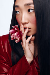 Portrait of a woman with long black hair and red jacket holding a flower in front of her face