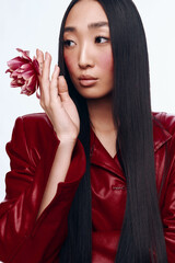 Beautiful young woman with long black hair and red leather jacket holding a flower in hand