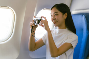 Young Asian woman traveler sitting near window and looking out window holding notebook on airplane,...