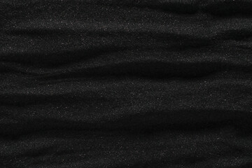 Dunes of dark black sand. Stripes and ripples of smooth volcanic sand texture or wallpaper. Wave pattern in black sand background.