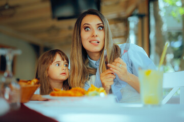 Cheerful Mother Eating Lunch with her Toddler Daughter. Happy family sitting in a restaurant...