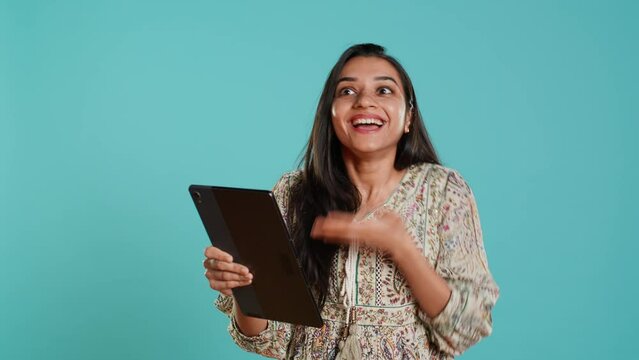 Cheerful woman gossiping with friends during videoconference meeting using tablet, studio background. Jolly person bonding with mates, spreading rumors during online videocall on device, camera A