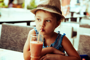 Cute caim thinking kid girl in summer hat drinking tasty juice in street restaurant. Closeup