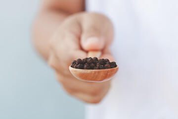 The male hand holding a wooden spoon full of pepper spices, composition isolated over the white background. Peppercorns and black pepper in a Wooden spoon.