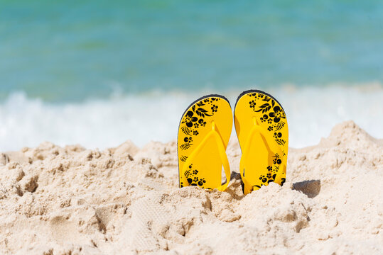 Yellow Sandal rubber shoe on the beach vacation time to travel. Tropical summer beach with sea wave in sunshine day. Slipper shoes outdoor with white wave blue sea on the beach. Summer tropical beach