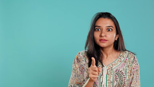 Annoyed indian woman doing shushing hand gesturing, irritated by noise, having negative mood. Person placing finger on lips, doing quiet sign gesture, isolated over studio background, camera B