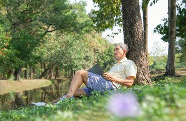 asian senior man fell asleep while reading a book under a tree,older adult resting in the nature park,concept of elderly people lifestyle,hobbies,relaxing in nature