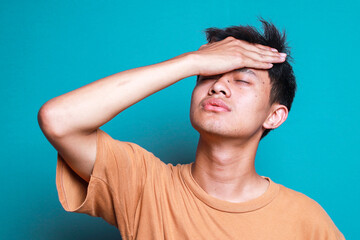 Sleepy and Tired Young Man Touching Forehead Feeling Bored and Lazy Isolated on Blue Background. 