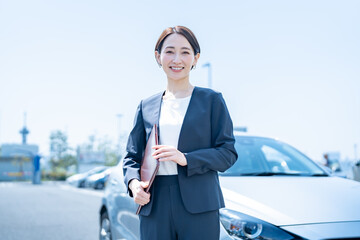 屋外に停めてある車の前に立つスーツを着た女性