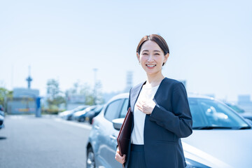 屋外に停めてある車の前に立つスーツを着た女性