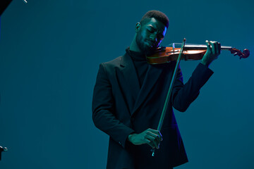 Elegant man in suit performing on violin in front of blue illuminated background for music concept