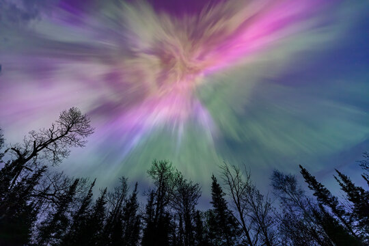 Northern lights erupt over a lake in Minnesota in a dark sky overhead shining rainbow of Aurora light