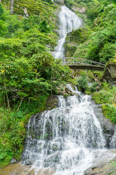 A waterfall cascading through a green forest and under a footbridge at Sapa in Vietnam