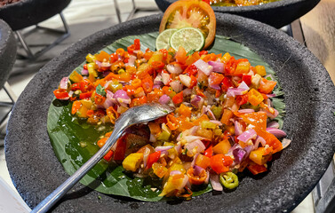Spicy condiment of Indonesian sambal dabu dabu made of chilli, tomato and shallot with lemon basil in a ceramic bowl, wooden spoon on grey background