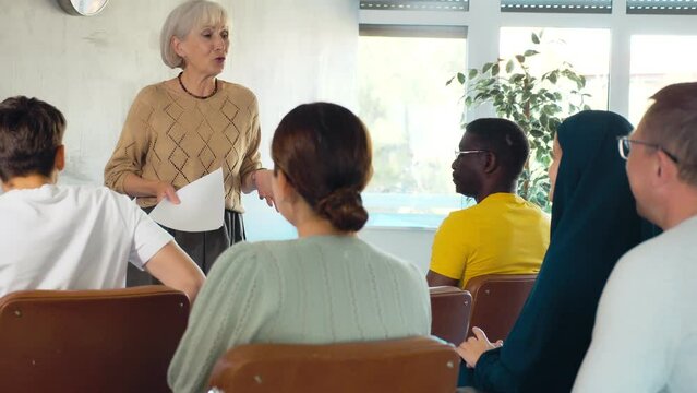 Mature female teacher giving lecture to group of multinational students in classroom. High quality 4k footage