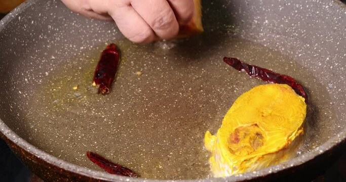 Frying hilsa fish cut pieces  Asian Bengali cooking oil with salt yellow turmeric cumin spice bubbling splash