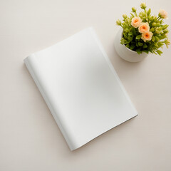 A white notebook sits on a table next to a vase with flowers