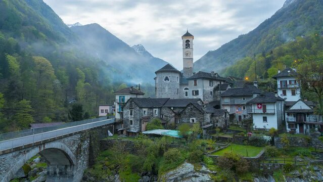 Old church between forests and mountains with a stone bridge at dusk with fog. The clouds gather, the lamps come on. Nature is enchanting