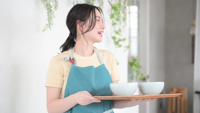 カフェで配膳するエプロン姿の接客業の女性か主婦のイメージ　いらっしゃいませ
