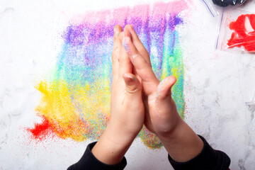 Little fingers playing with vibrant sand on white background. Motor skills, child creativity concept