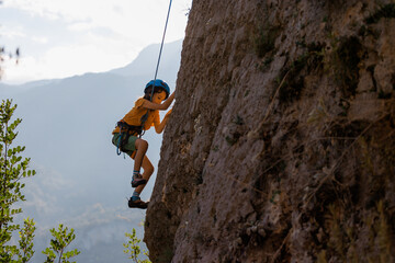 Children's rock climbing. A boy climbs a rock against the backdrop of mountains. Extreme hobby....