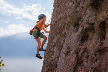 rock climber boy. child is practicing rock climbing. summer camp. sport in nature. cute teenager climbing on a rock with belay