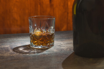 A glass of whiskey sits on a table next to a bottle. The glass is half full. Concept of relaxation...