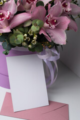 Fresh bouquet of pink flowers with a greeting card. Orchids and eucalyptus in a round box. Postcard template for text, photo, illustration, logo. Flower shop. Flower delivery