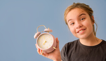 A girl is holding a pink alarm clock with the time of 08:00
