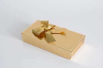 A gold box with a gold ribbon tied around it. The box is sitting on a white background