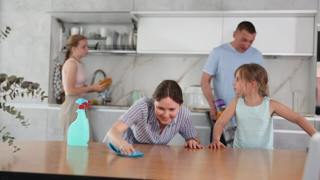 Dreamy smiling teenage girl engaged in household cleaning together with family, wiping table in kitchen immersed in pleasant thoughts. High quality 4k footage