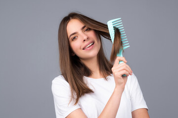 Portrait of beautiful young woman combing her hair, smiling. Female brushing healthy hair with comb.