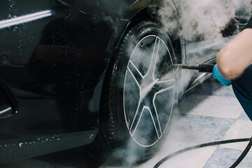 Person washing a car with a high-pressure sprayer in a garage