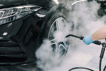 Person washing a car with a high-pressure sprayer in a garage