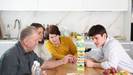 Happy young girl concentrating on removing block from tower while playing jenga, spending free time with boy-friend or husband and parents at light family home 