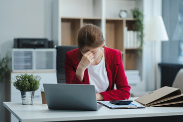 Young sad businesswoman is sitting at table, covering his face. On desk is laptop, tablet computer,...