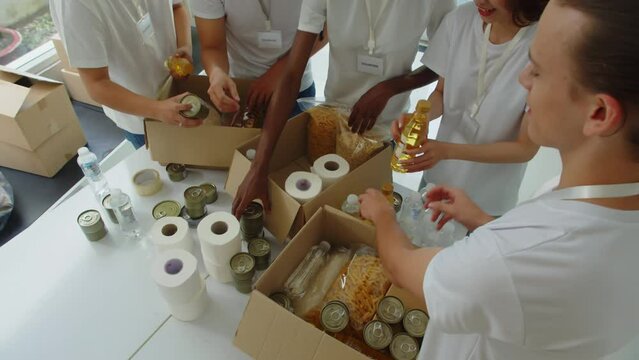 Cropped shot of young group of people packing cardboard box with food and toiletry for donation in center