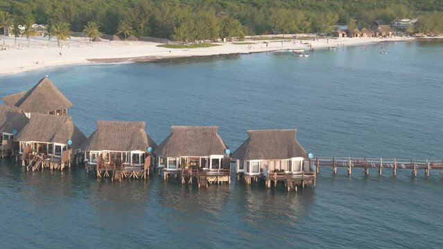 Aerial view orbiting luxurious thatched roof Kae Funk chalets Indian ocean beach resort in Zanzibar Chwaka bay
