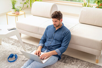 Confident man sitting on the floor at home and using his laptop