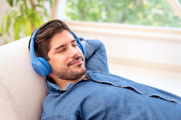 A man with headphone relaxing on the sofa at home and listening to music