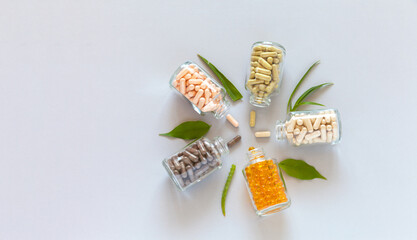 Top view of glass vials with capsules of food bio additives and green plants on light background....
