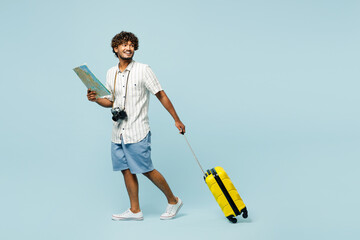 Full body happy traveler Indian man in white casual clothes hold bag read map isolated on plain blue background Tourist travel abroad in free spare time rest getaway Air flight trip journey concept