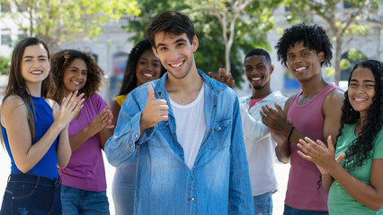 Latin american male young adult showing thumb up with group of applauding people