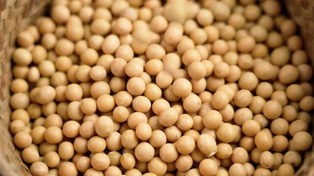 Organic soy beans falling into a rustic wicker bowl. Raw dried soya grains. Healthy legume ingredient. Slow motion. Rotation